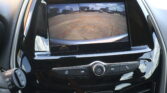 Display of a car's rearview camera with orange guiding lines over a parking lot scene, aiding reverse parking.