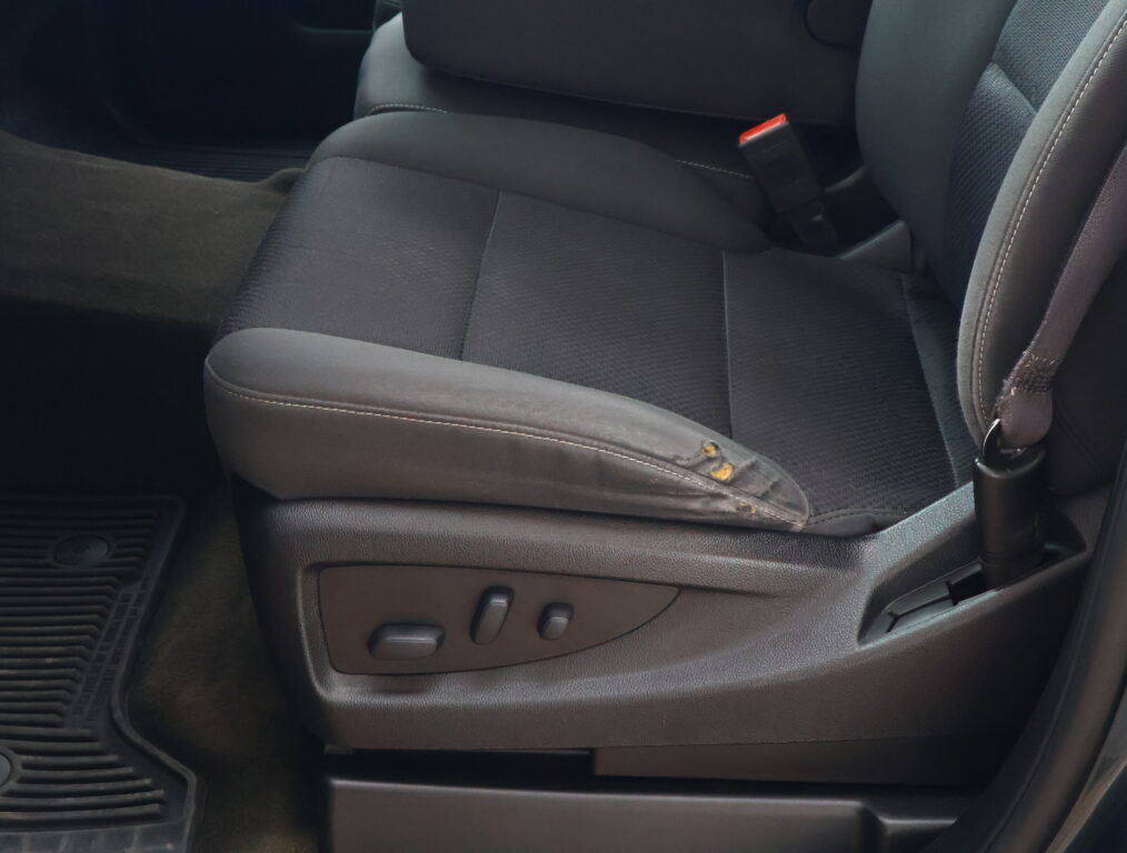 Close-up of a dark gray car seat with power adjustment controls on the side and a visible red seatbelt buckle nearby.
