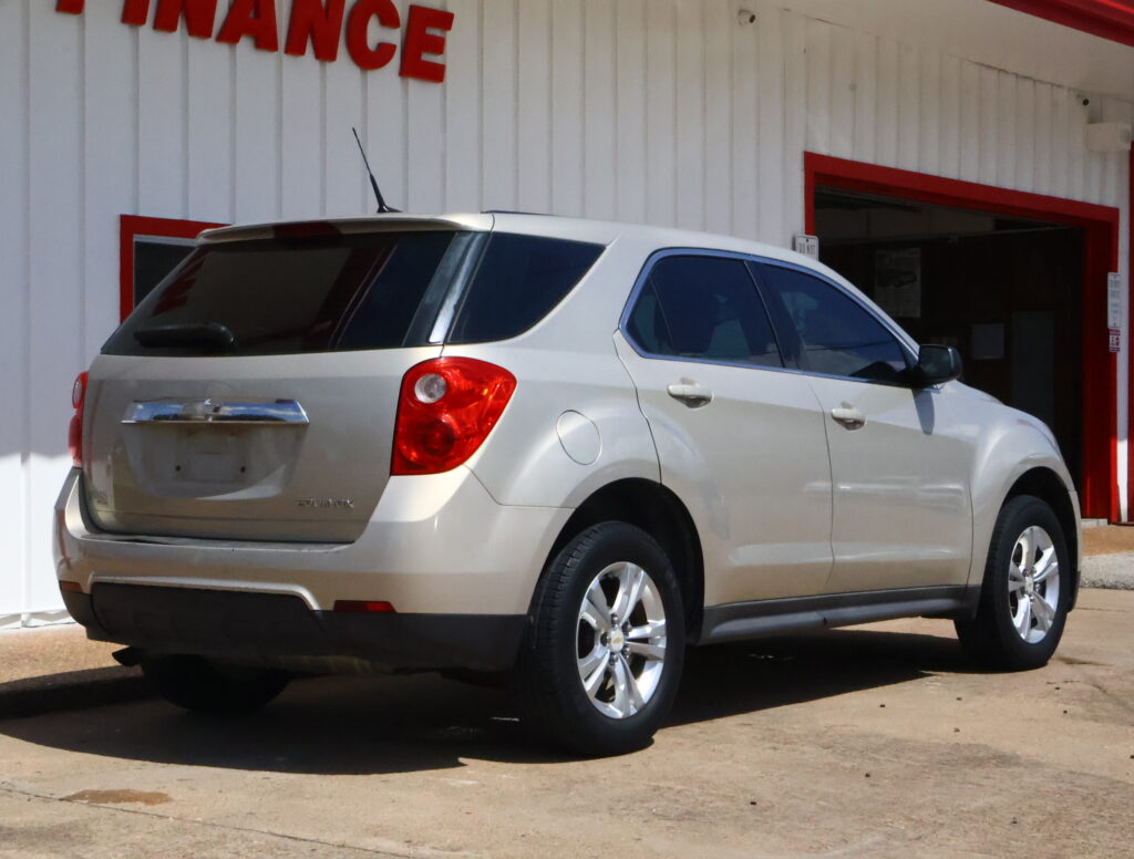 Rear three-quarter view of a silver SUV parked in a driveway beside a white building with red trim and an open garage door in the background