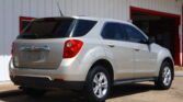 Rear three-quarter view of a silver SUV parked in a driveway beside a white building with red trim and an open garage door in the background