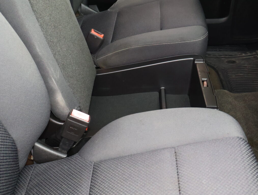 Gray fabric car seats with visible red seatbelt buckles and center console nearby showing the seating area and floor mats.