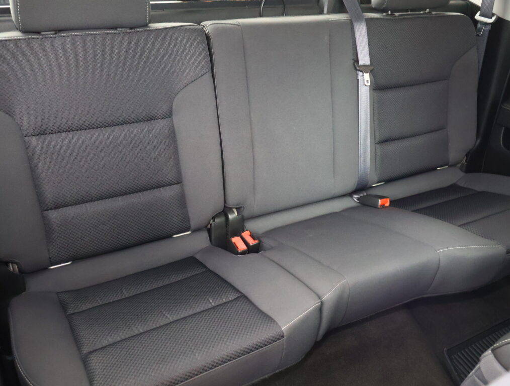 Rear car seat with three cushions in dark fabric and visible seat belts and buckles.