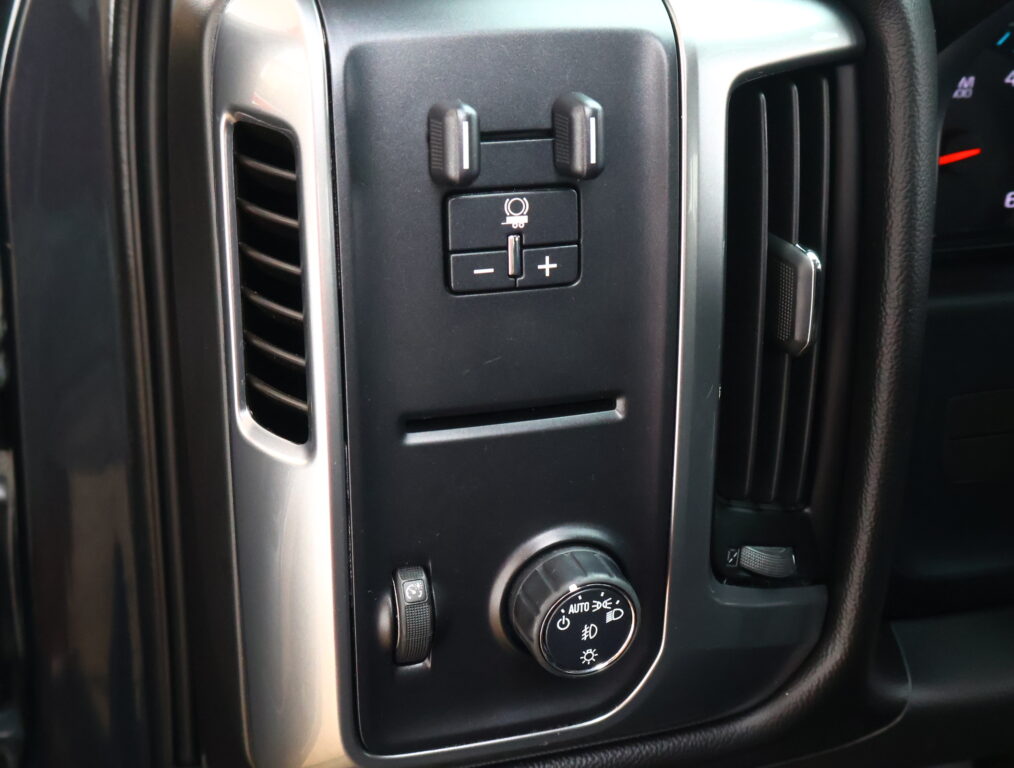 Close-up of a vehicle center console: two small vertical toggles above a square button with a circular icon and a plus/minus pair below.