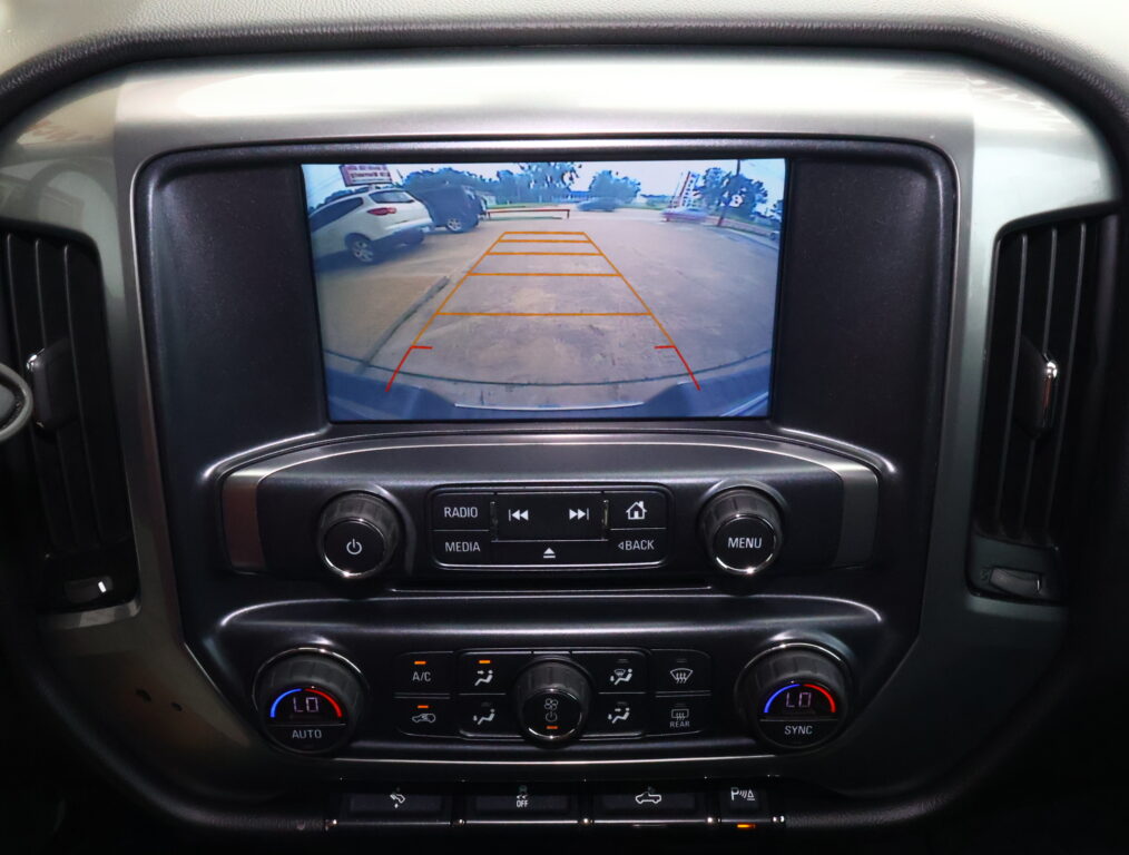 Car rearview camera display with orange guide lines showing a parking space in a lot.