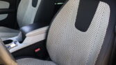 Interior of a car showing perforated light-gray seats with black sides and red stitching along the edges. Center console with cup holder visible.