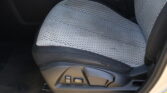 Front car seat with light gray perforated upholstery and red stitching; adjustment controls on the side edge.