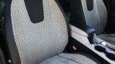 Front and center interior of a car showing light gray perforated seat upholstery with black sides and red stitching