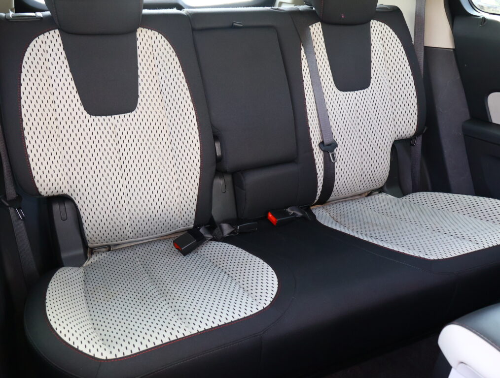 Rear car seats with light perforated fabric and black edges, red stitching visible.