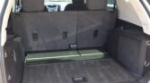 Interior of an SUV with the third-row seats upright, showing a spacious cargo area and black carpeting behind them.