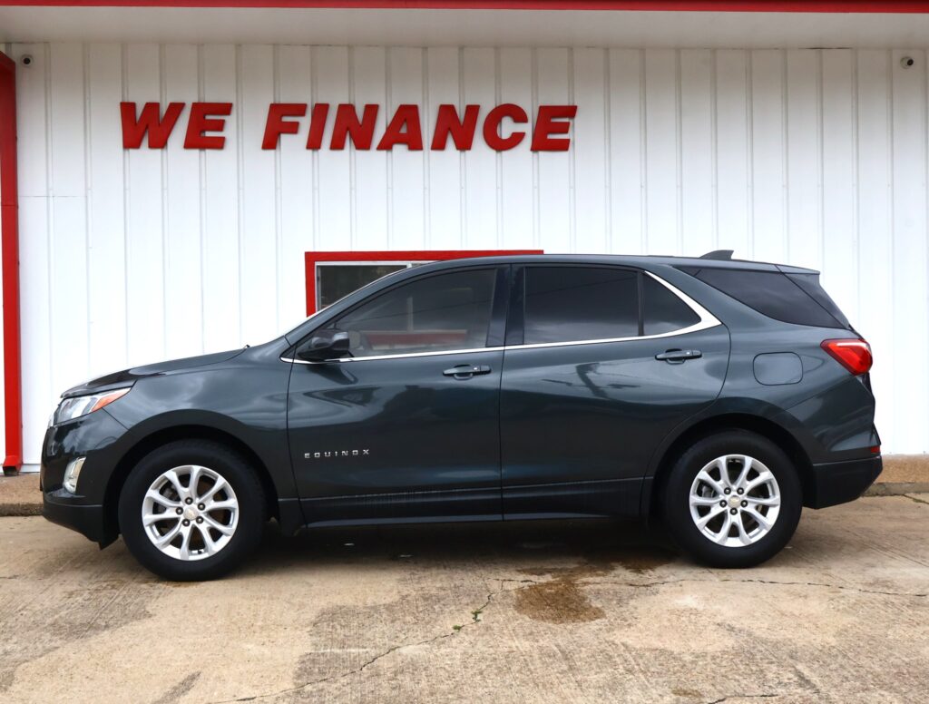 Grey Chevrolet Equinox parked in front of a white wall with a red 'WE FINANCE' sign.
