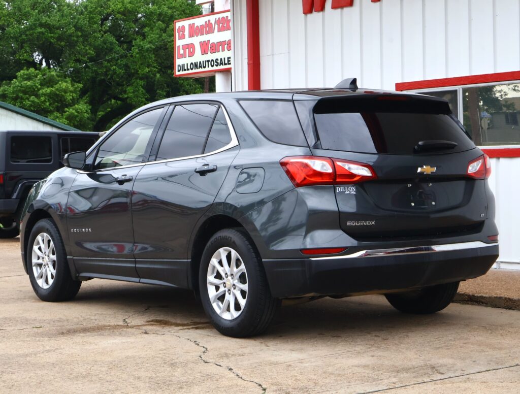 Gray Chevrolet Equinox SUV parked outside a car dealership with a red-and-white sign in the background reading DILLON AUTO SALE.