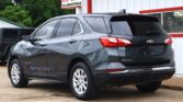 Gray Chevrolet Equinox SUV parked outside a car dealership with a red-and-white sign in the background reading DILLON AUTO SALE.