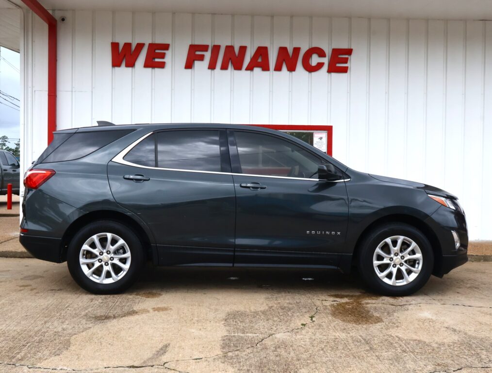Dark gray Chevrolet Equinox parked in front of a white building with a large red 'WE FINANCE' sign above it, dealership scene