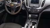 Interior view of a car cabin: steering wheel with Chevrolet logo, central touchscreen, gear shifter, and cup holders in a black dashboard area.