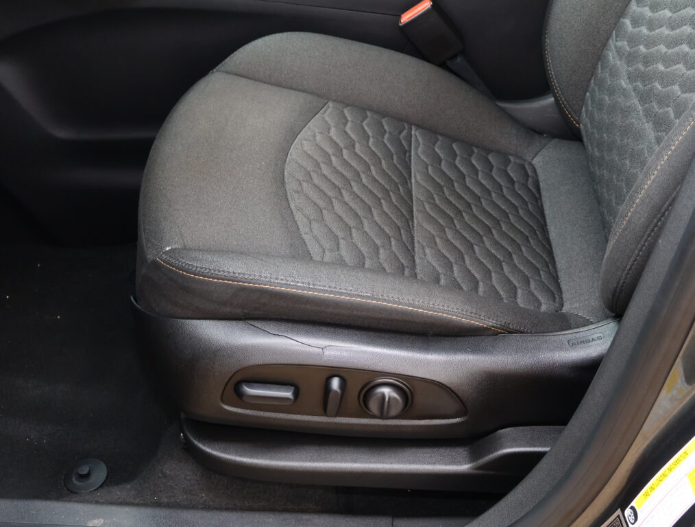 Front driver's seat inside a car, showing quilted dark fabric with orange-stitch detailing and the seat adjustment controls on the lower side edge.