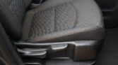 Front car seat with dark quilted fabric and orange stitching, showing the seat and nearby seat belt buckle.