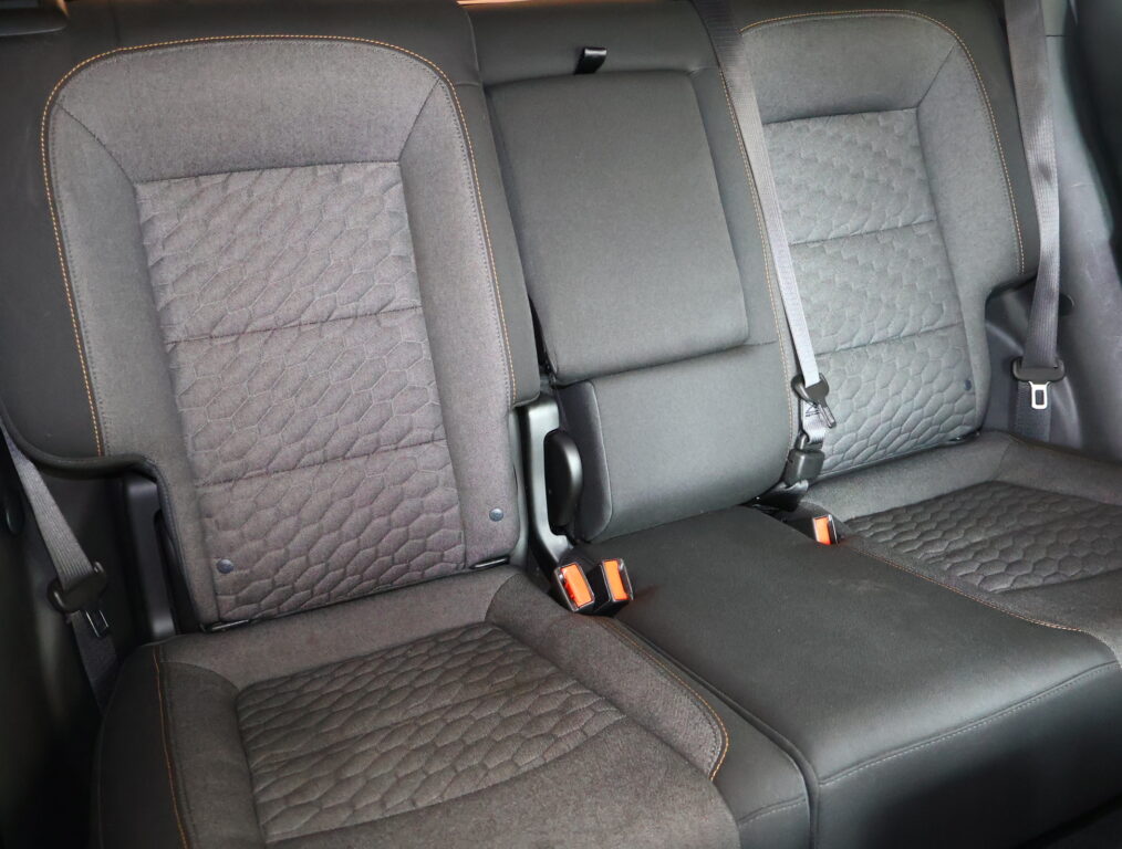 Rear car seat row with dark fabric upholstery, orange contrast stitching, and visible seat belts.