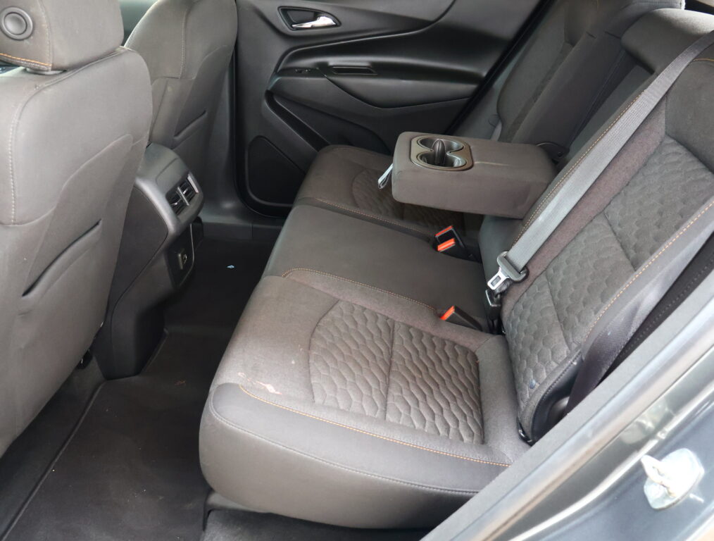 Rear passenger seats in a dark fabric car, center armrest folded down with built-in cup holders