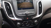 Center console screen showing a rear-view camera view with parking guidance lines in a parking lot, flanked by air vents and control buttons.