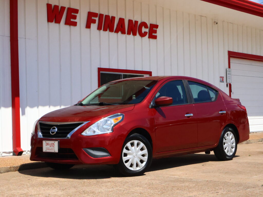 Red Nissan sedan parked in front of a white building with bold red 'WE FINANCE' letters on the wall.