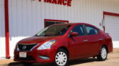 Red Nissan sedan parked in front of a white building with bold red 'WE FINANCE' letters on the wall.