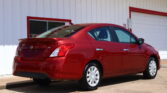 Red Nissan Versa parked in front of a white building with red trim and a partially visible 'FINANCE' sign, shown from the rear side.