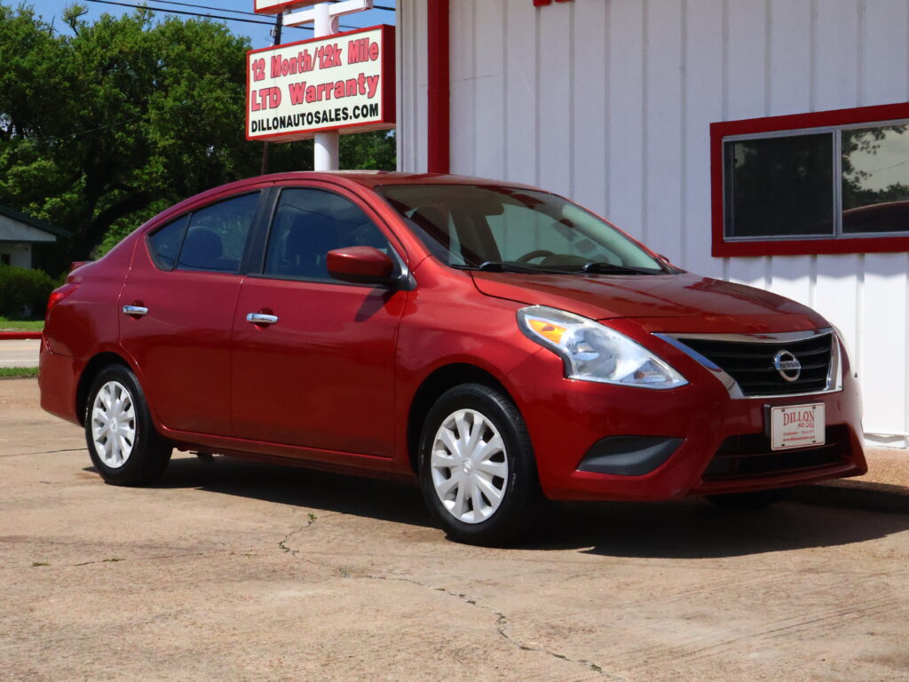 Red Nissan sedan parked in front of a white building with red trim and a Dillon Auto Sales sign in the background.
