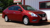 Red Nissan sedan parked in front of a white building with red trim and a Dillon Auto Sales sign in the background.
