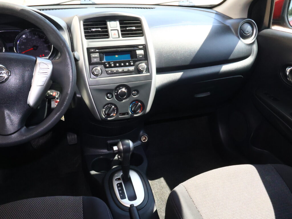 Interior of a car cockpit: steering wheel on the left, central dashboard with radio and climate controls, gear shift lever in the foreground, and front seats.