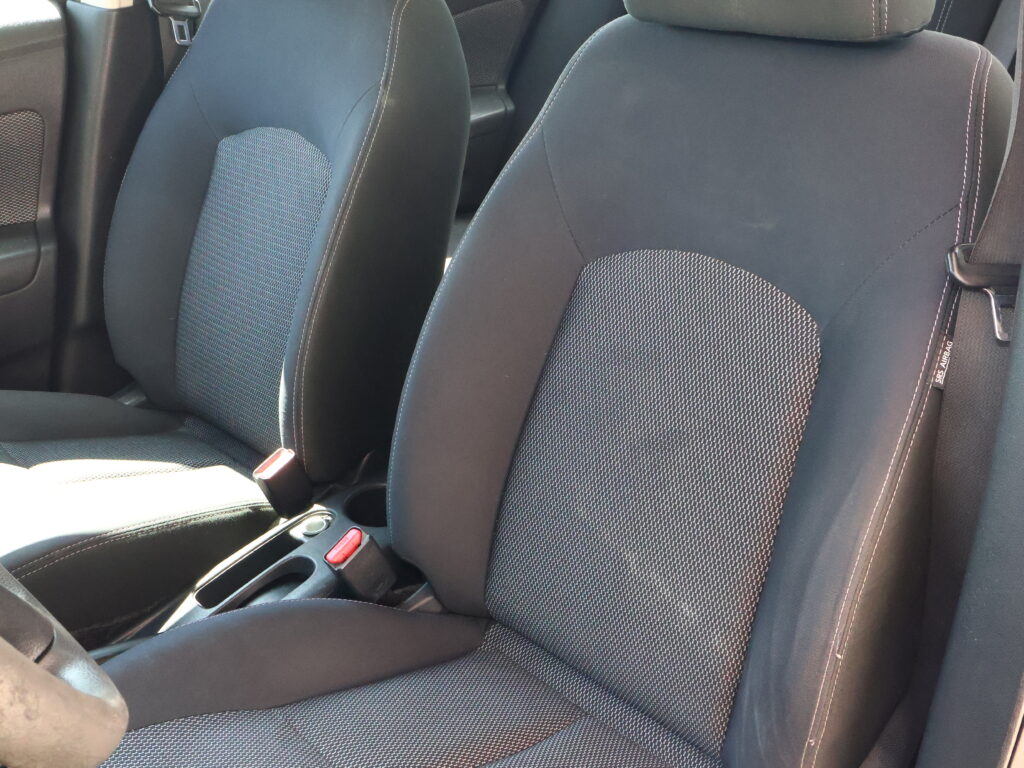 Front seats in a car with dark fabric upholstery and white stitching, center console visible between them.