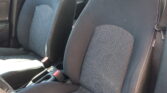 Front seats in a car with dark fabric upholstery and white stitching, center console visible between them.