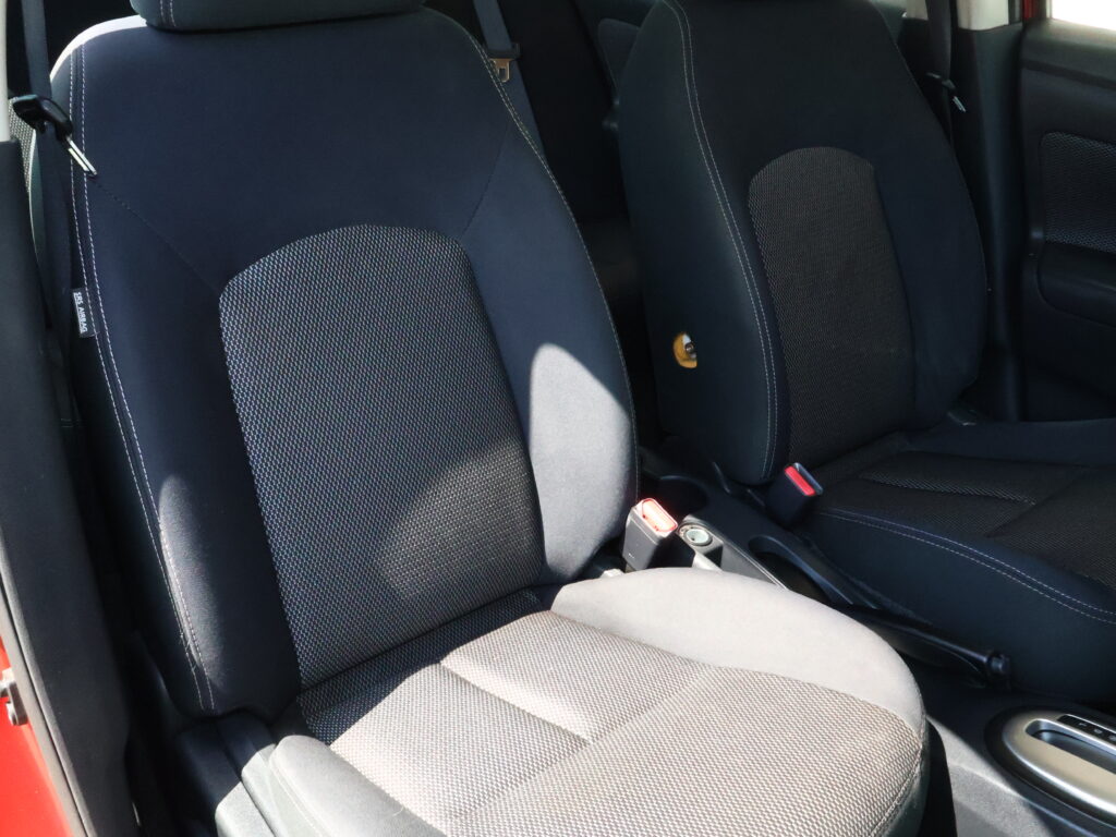 Dark car interior showing front seats with black fabric upholstery and dotted center panels, white contrast stitching.