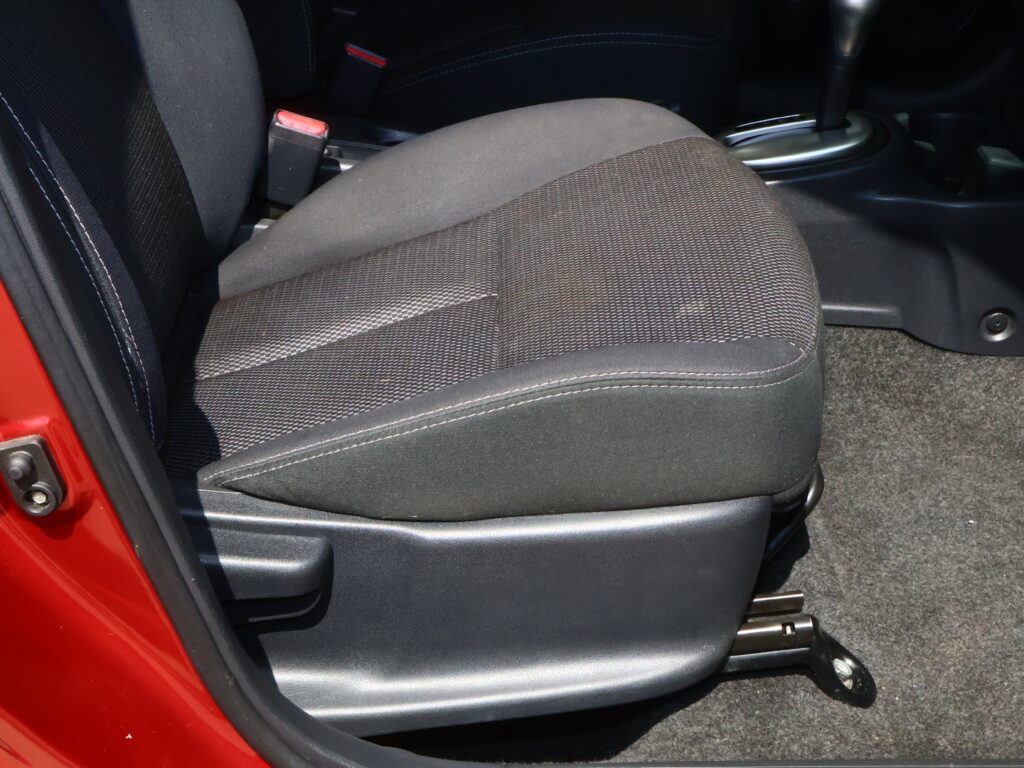 Front car seat with dark fabric upholstery, red seatbelt buckle, and center console visible next to the gear lever on a car floor.