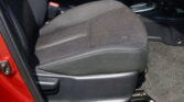Front car seat with dark fabric upholstery, red seatbelt buckle, and center console visible next to the gear lever on a car floor.