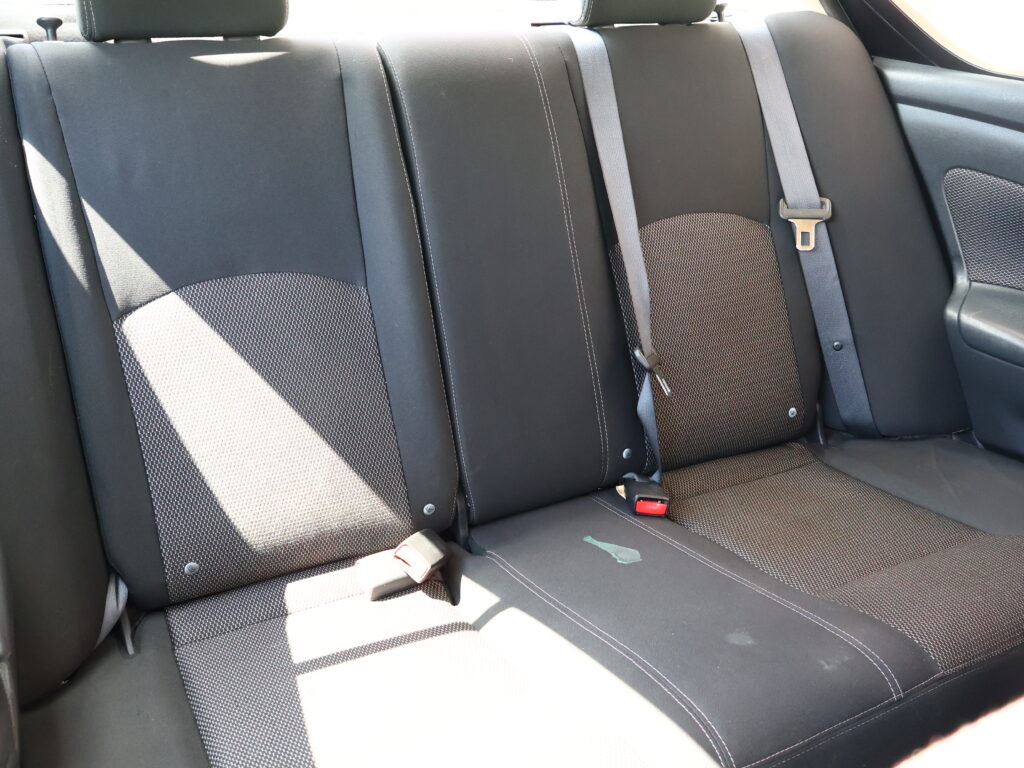 Back seat of a car with dark fabric upholstery, three seating positions, and visible seat belts and buckles.