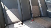 Back seat of a car with dark fabric upholstery, three seating positions, and visible seat belts and buckles.