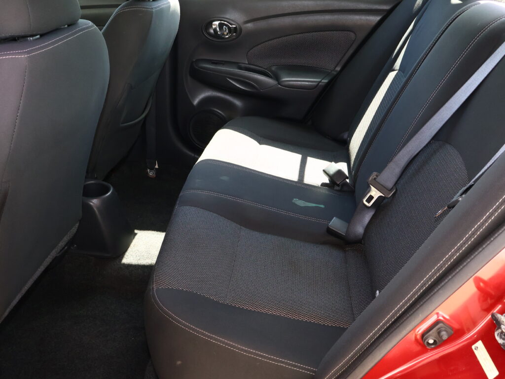 Backseat of a car with dark fabric seats and light stitching, visible seat belts and door panel.