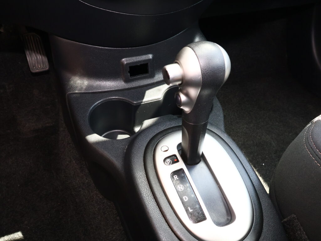Close-up of a car's automatic shifter with P R N D gear indicators visible and a surrounding center console area.