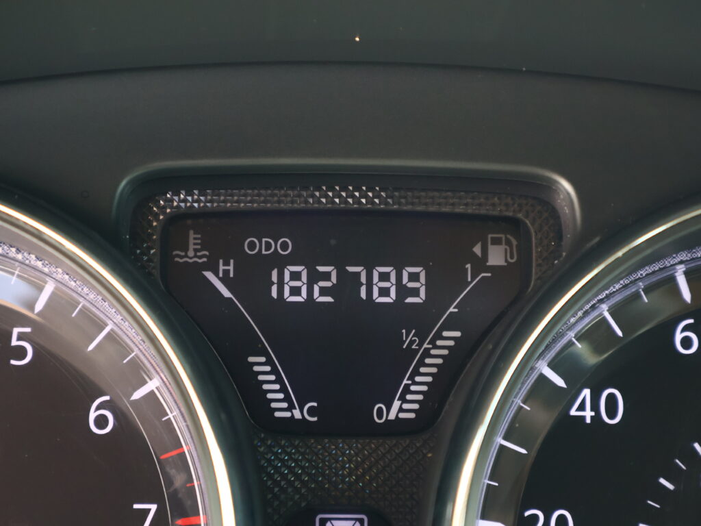 Close-up of a car dashboard instrument cluster showing the speedometer, fuel gauge, and temperature indicators in white on black.