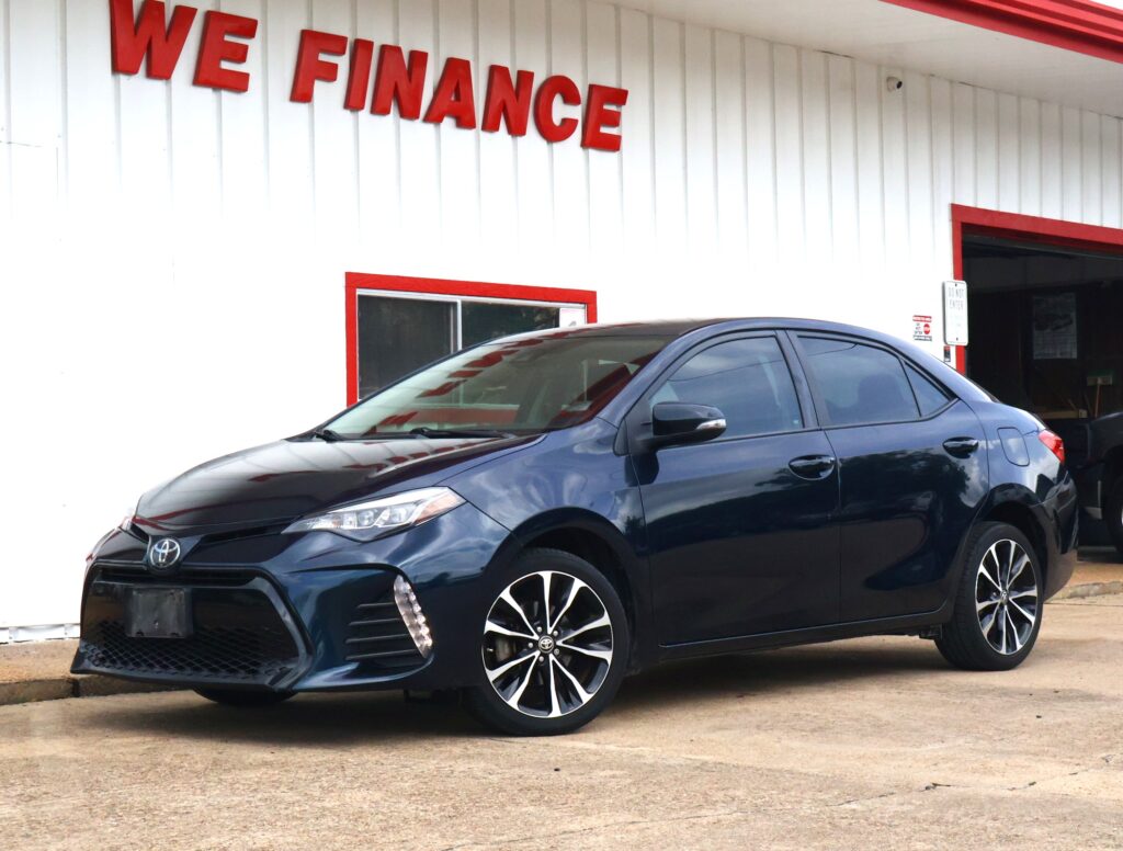 Blue Toyota sedan parked outside a white building with red trim and a large red sign reading 'WE FINANCE' above the entrance (informative storefront scene).