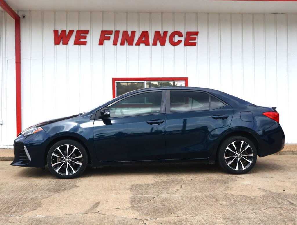 Blue sedan parked in front of a white wall with a red 'WE FINANCE' sign above it at a car lot.