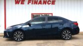 Blue sedan parked in front of a white wall with a red 'WE FINANCE' sign above it at a car lot.