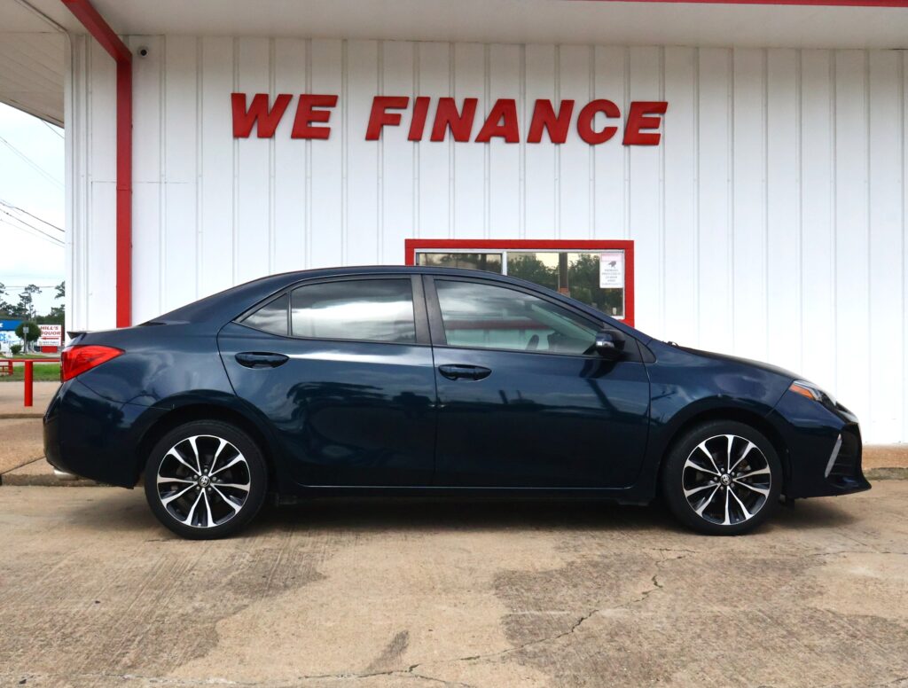 Blue sedan parked in front of a white building with large red letters reading 'WE FINANCE' on the wall behind it
