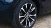 Close-up of a car wheel with a black and silver multi-spoke alloy rim and tire on a paved surface.