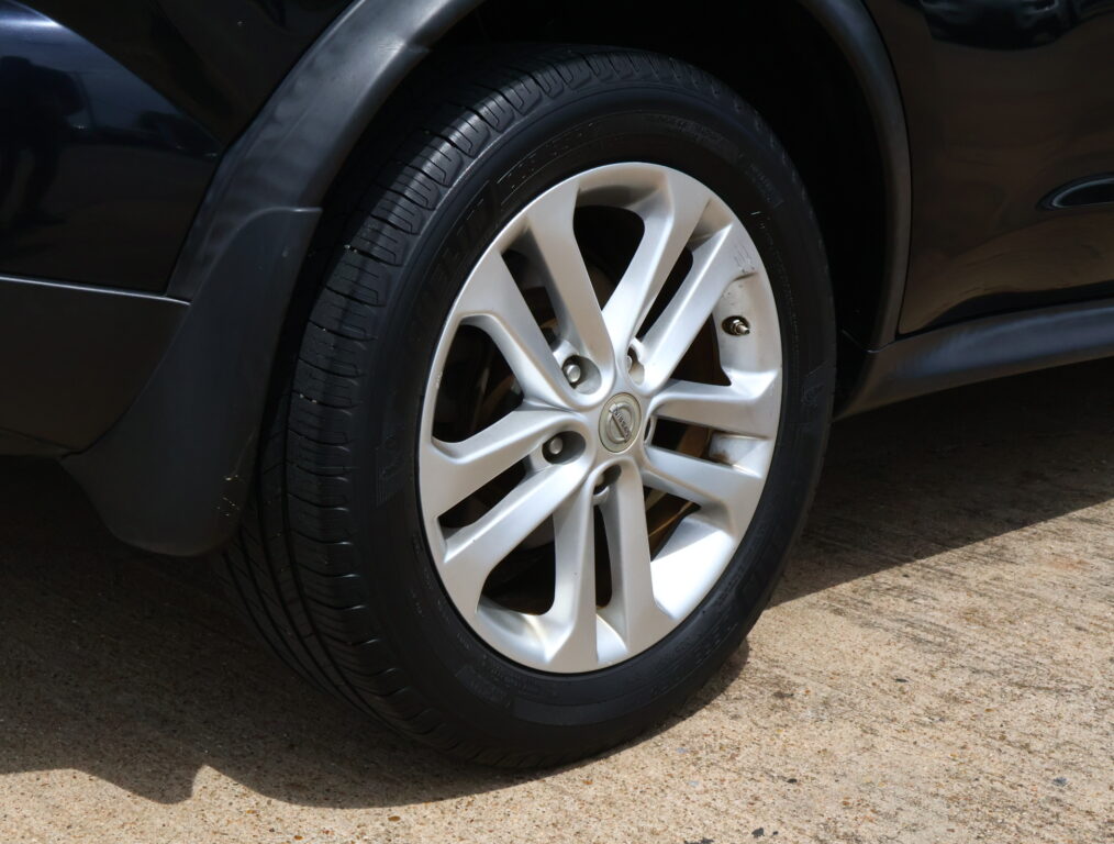 Close-up of a dark car's tire and silver alloy wheel with a Nissan emblem on the hub.