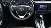 Steering wheel in a car interior with a digital instrument display and a touchscreen center console to the right of the wheel