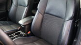 Interior of a car showing black leather front seats with blue stitching and a center console between them, with seat belts visible.