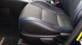 Close-up of a car's front passenger seat and center console, showing black upholstery with blue piping and a red seatbelt buckle nearby.