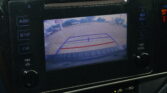 Rearview camera display on car screen with parking guidelines over a driveway scene (blue lines and red line).