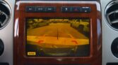 Car dashboard center screen showing the rearview camera view with parking guide lines in a parking lot.